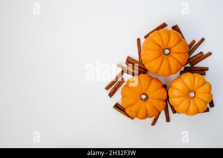 three small orange pumpkins with cinnamon sticks top view flat lay. Halloween and Thanksgiving autumn concept Stock Photo