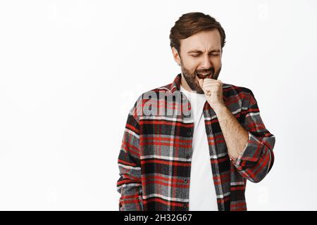 Image of bearded guy yawning, cover mouth yawn, falling asleep, standing over white background Stock Photo