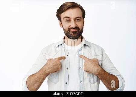 This is me. Smiling confident guy with beard, pointing at himself with self-assured macho expression, self-promoting, standing over white background Stock Photo