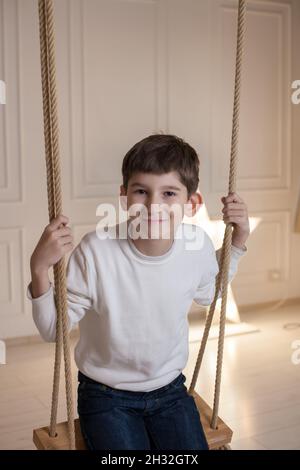 Cute happy kid with toothy smile holding ropes on the swing chair Stock Photo