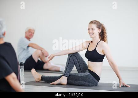 Happy young woman sitting on the mat and practicing yoga in the class Stock Photo