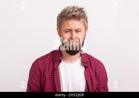 Portrait of desperate young man with beard sadly looking at camera and frowning, pursing lips, feeling regret or upset. Indoor studio shot isolated on gray background Stock Photo