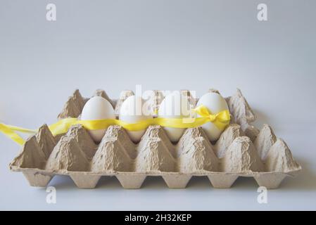 White eggs with yellow gift ribbon in an egg carton on a white background. Stock Photo