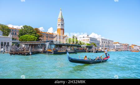 VENICE, ITALY - AUGUST 02, 2021: Tourists on gondola and Venice cityscape with St Mark Campanile, Italian: Campanile di San Marco, on background Stock Photo