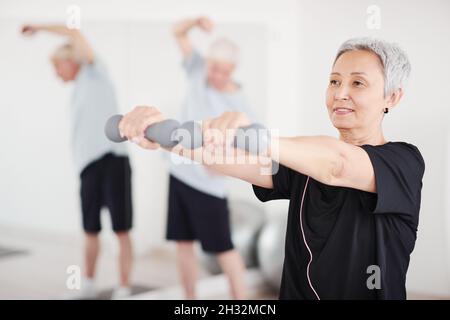 Mature woman exercising with dumbbells during sports training in the studio Stock Photo