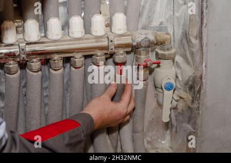 Repair and service concept heating systems. Specialist inspects floor heating system. Adult male checks the tightness of the pipes on the water manifo Stock Photo