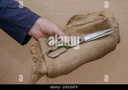 xvOld scissors, sackcloth in hand. A grown man's hand holds the rough cloth and old scissors. Close-up.  Selective focus Stock Photo