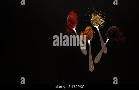 Different spices in spoons on black background Stock Photo