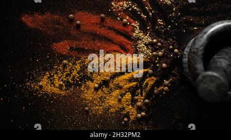 Different spices are scattered near the mortar on black background Stock Photo