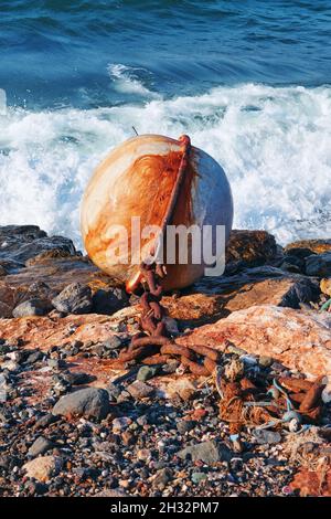 Big rusty white round buoy and chain on the shore with sea background. Stock Photo