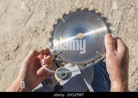 a man removes the plastic protection from the saw blade teeth on a circular miter saw for installation and replacement. Stock Photo