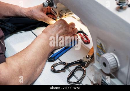 Female hands sewing fabric with professional sewing machine at the tailor shop. Stock Photo