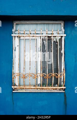 House window with rusty wrought iron bars or lattice with blue walls. House security. Stock Photo