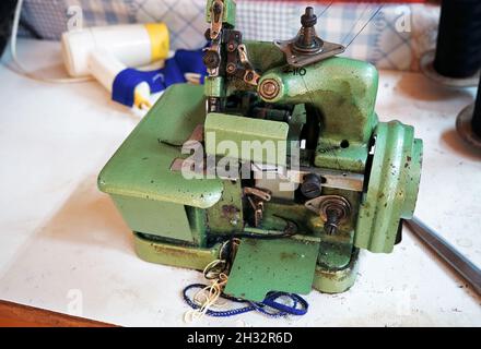Old vintage metal overlock machine on the workbench of a traditional tailor shop. Stock Photo