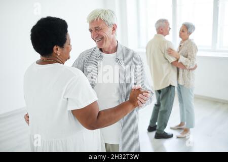 Two senior couples smiling to each other holding hands while dancing a slow dance in dance studio Stock Photo
