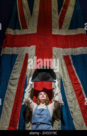 London, UK. 25th Oct, 2021. A Bicorne Hat, believed to Have Been Worn by Napoleon Bonaparte, attributed to Poupart & Cie, Paris, Circa 1806-07, Estimate: £100,000-150,000 in front of a Giant Battle Flag (Union Jack) from HMS Temeraire, which fought at Trafalgar, est £5,000-10,000 -Preview of the Napoleon Bonaparte: The British Sale at Bonhams New Bond Street, London. The sale is on 27 October. London, UK. 25 Oct 2021. Credit: Guy Bell/Alamy Live News Stock Photo