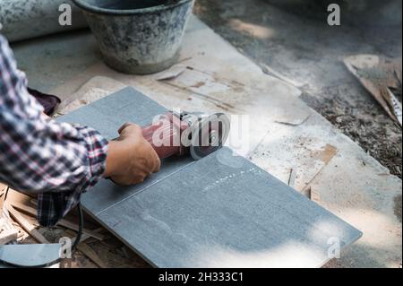 Worker using electric circular saw cutting granite tile in construction site Stock Photo