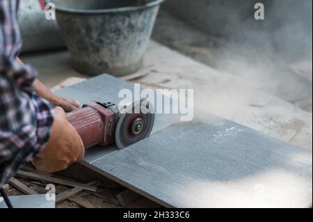 Worker using electric circular saw cutting granite tile in construction site Stock Photo