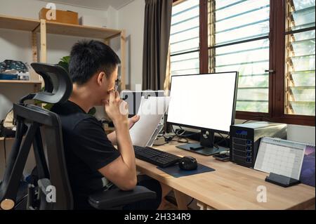 Freelance young asian man working and examining paperwork and empty display, storage box, calendar at wooden table on window side in the house Stock Photo