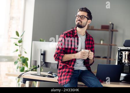 Portrait of nice attractive dreamy cheerful guy drinking coffee working company good morning at work place station indoors Stock Photo