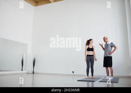 Senior man discussing sports training together with his young coach while they standing in sport gym during personal training Stock Photo