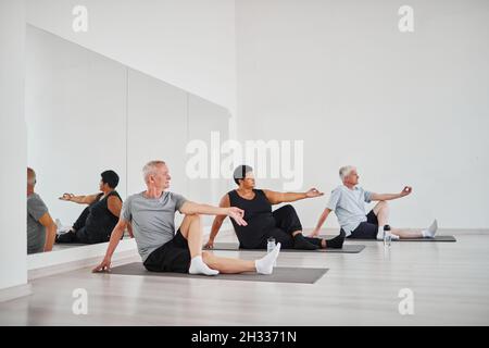 Group of senior people exercising on exercise mat and meditating during yoga class in studio Stock Photo