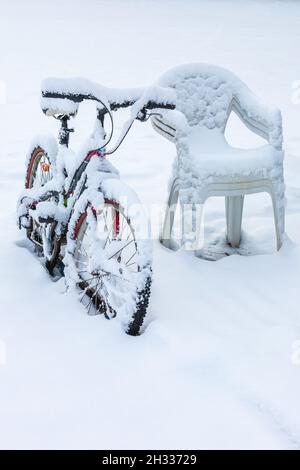 Snow covered bicycle by some chairs in winter Stock Photo