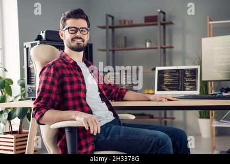 Portrait of attractive cheerful skilled guy technician manager sitting in chair creating web design indoor at work place station Stock Photo