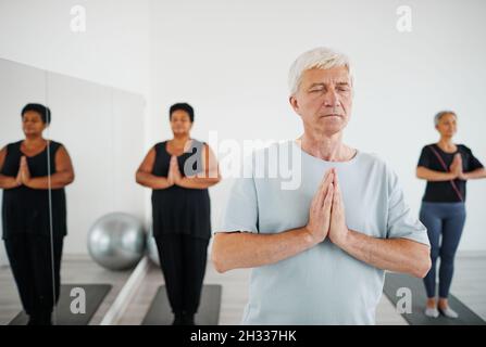 Portrait of senior man with eyes closed practicing meditation during group yoga class Stock Photo