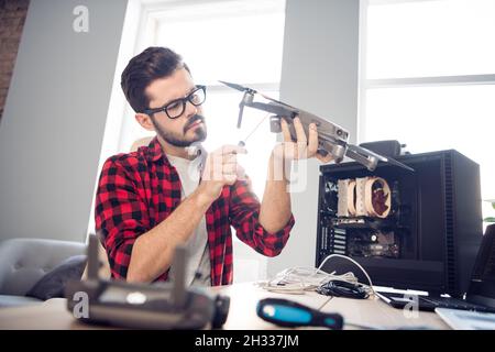 Portrait of attractive serious focused skilled guy holding in hands drone fixing detail service support at work place station indoors Stock Photo