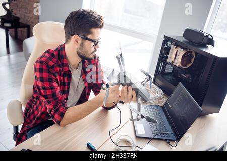 Portrait of attractive clever smart focused guy fixing drone bug software programming code security data at work place station indoors Stock Photo