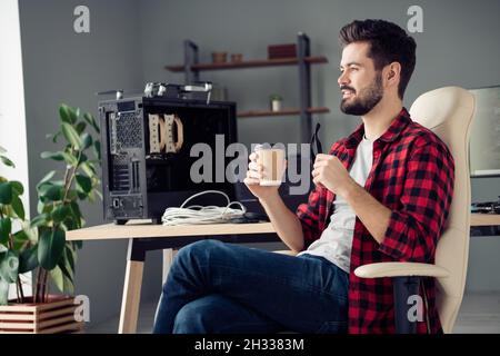 Profile side view portrait of attractive intellectual cheerful dreamy guy hacker drinking latte at work place station indoors Stock Photo