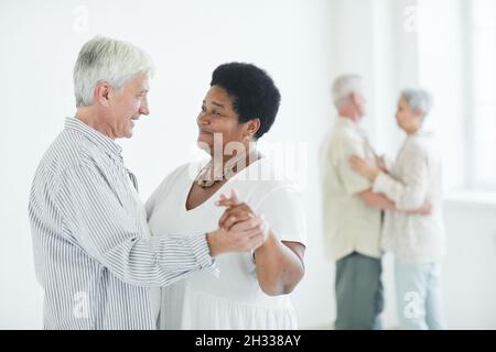 Senior couple enjoying dance together looking at each other, they learning to dance in studio with other couple in the background Stock Photo