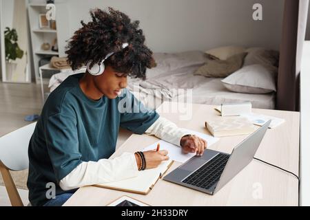 Portrait of African-American teenage boy studying at home or in college dorm and using laptop, copy space Stock Photo
