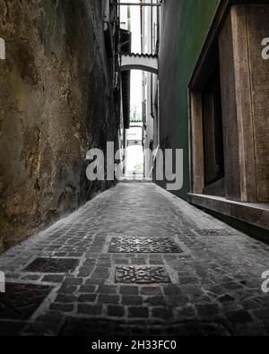Empty narrow alley between two old grungy dirty stone buildings in Garda, Italy Stock Photo