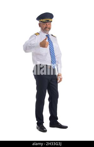 Cheerful airline pilot wearing uniform with epaulets showing thumb up gesture of approval, standing isolated on white background. Stock Photo
