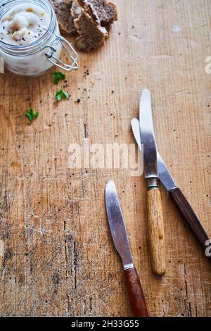 Vertical top view set of stainless knives on a table with a glass jar of lard spread and bread Stock Photo
