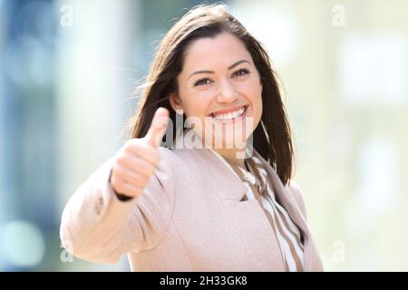 Happy businesswoman standing in the street with thumbs up looking at camera Stock Photo