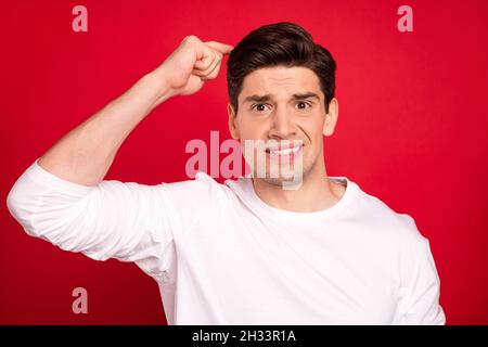 Photo of think brunet millennial guy finger head wear white shirt isolated on red color background Stock Photo