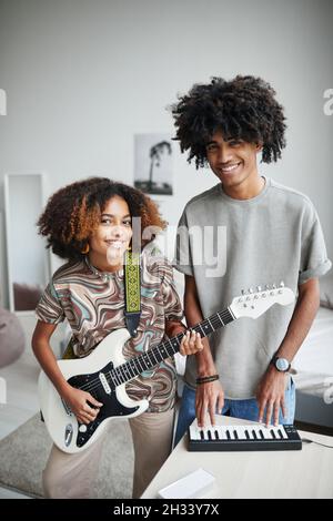 Vertical portrait of two African-American young people playing music at home and smiling at camera, brother and sister Stock Photo