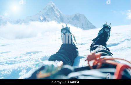 POV shoot of a high altitude mountain climber's lags in crampons. He lying and resting on snow ice field with Ama Dablam (6812m) summit covered with c Stock Photo
