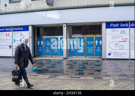 Slough, Berkshire, UK. 25th October 2021. Shoppers walk past Covid-19 prevention measure signs in Slough High Street. The number of positive Covid-19 cases in Slough have risen to 480 from 419 per 100,000 people in the seven days up to and including 18 October compared with the week before . Credit: Maureen McLean/Alamy Live News Stock Photo