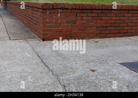 Very low view of a red brick retaining wall at the intersection of two sidewalks, cracked concrete creative copy space, horizontal aspect Stock Photo
