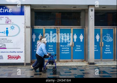 Slough, Berkshire, UK. 25th October 2021. Shoppers walk past Covid-19 prevention measure signs in Slough High Street. The number of positive Covid-19 cases in Slough have risen to 480 from 419 per 100,000 people in the seven days up to and including 18 October compared with the week before . Credit: Maureen McLean/Alamy Live News Stock Photo