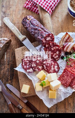 Vertical top view of dry-cured sausages with cheese on a wooden cutting board with knives on a table Stock Photo