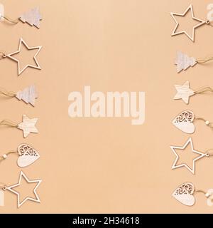 Frame of two vertical rows of Christmas festive craft decorations - wooden stars, Xmas trees, hearts on beige background with copy space in center. To Stock Photo