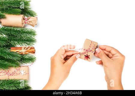 flat lay of woman hands tying bow of red rope on gift box for Christmas greetings, decor of Christmas trees on white isolated background Stock Photo