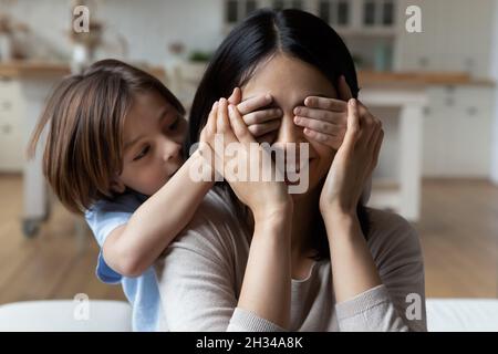 Playful kid covering mom eyes with hands, preparing surprise present Stock Photo