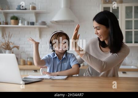 Excited schoolkid in headphones giving high five to happy mom Stock Photo