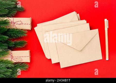 mockup blank stacks of paper craft envelopes and craft pen on red insulated background with spruce twigs and gift packages Stock Photo